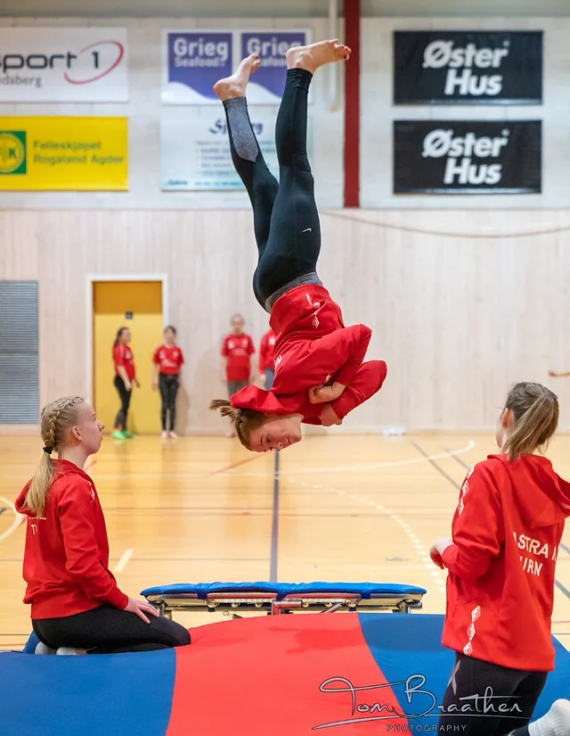 Turnjente i rødskjorte hopper og to andre jenter som sitter